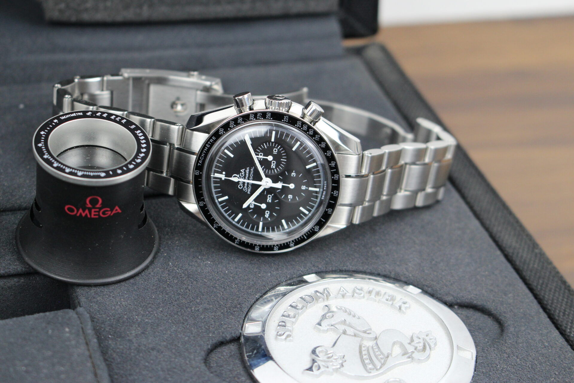 Omega Speedmaster Moonwatch Professional in it's box with a magnifying loupe and Omega paperweight